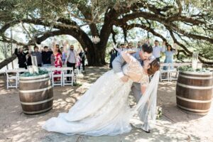 Houston bride with flowing chapel‑length veil walking toward the lakefront ceremony site at Pine Lake Ranch.
