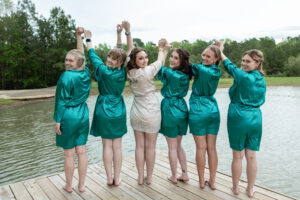 Guide to Planning a 4th of July Fireworks Proposal in Houston 8 Bridesmaids wearing green matching pajamas pose with the beautiful bride at our lake wedding venue near Houston